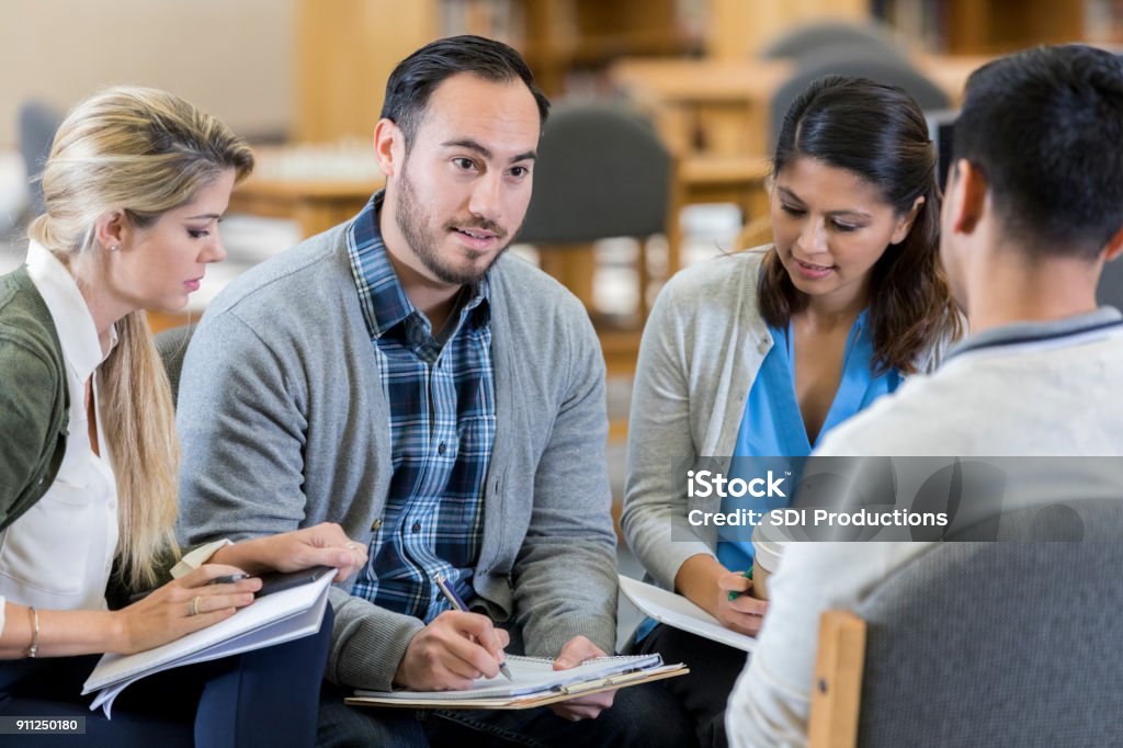 Counselor facilitates group therapy session Confident male counselor discusses something during group therapy session. Education Stock Photo