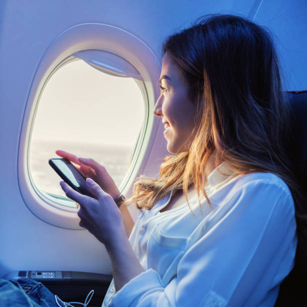 mujer utiliza teléfono inteligente mientras que en avión - silla al lado de la ventana fotografías e imágenes de stock