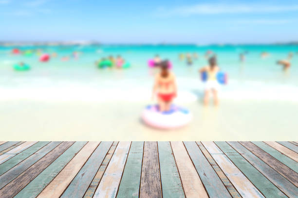 istock Wood table top with blurred people at the beach 911263106