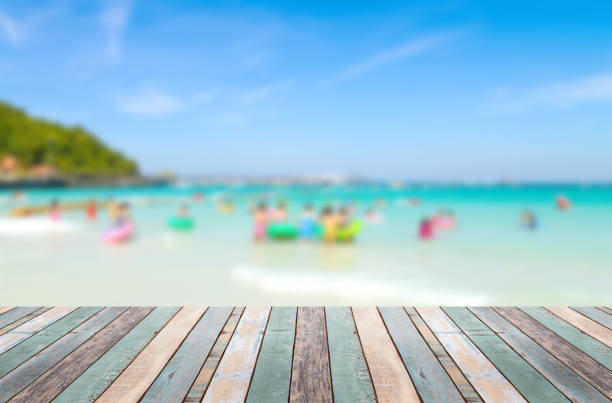 istock Wood table top with blurred people at the beach 911263110