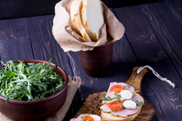 istock Sandwiches with ham, arugula and quail eggs on a serving board. Good breakfast or snack. Dark wooden background. 911278352