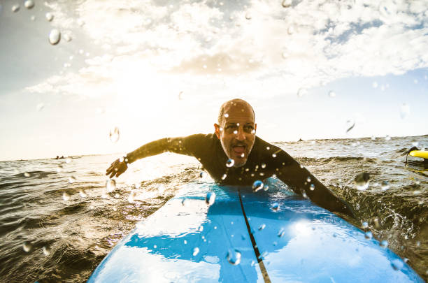 surfer facet brodzik z deski surfingowej o zachodzie słońca na teneryfie z nierozpoznawalnych ludzi na deskach surfingowych na tle - sport koncepcji podróży z płytkiej głębi ostrości z kroplami na obiektyw jako skład - paddling zdjęcia i obrazy z banku zdjęć