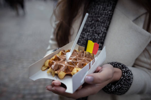 Belgian waffles decorated with the national flag in the young woman hands. Close up view. Hands holds fresh waffles with milk chocolate.