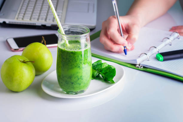 frau der rechten hand schreiben auf notebook und laptop, mobile smartphone in der nähe. gesundes getränk smoothie aus grünen spinat - spinach vegetable plant freshness stock-fotos und bilder