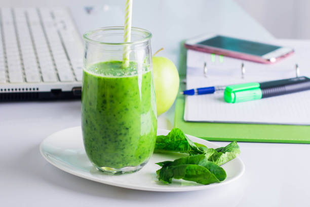 istock Workplace working table with laptop, computer, notebook, phone mobile smart phone, pen, marker. Healthy Drink Smoothie from Green Spinach and Apples 911344104