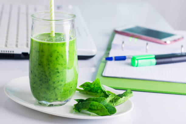 istock Healthy Drink Green Smoothie from Spinach on Workplace working table with laptop, computer, notebook, phone mobile smart phone, pen, marker. 911344108