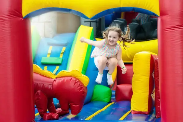 Child jumping on colorful playground trampoline. Kids jump in inflatable bounce castle on kindergarten birthday party Activity and play center for young child. Little girl playing outdoors in summer.