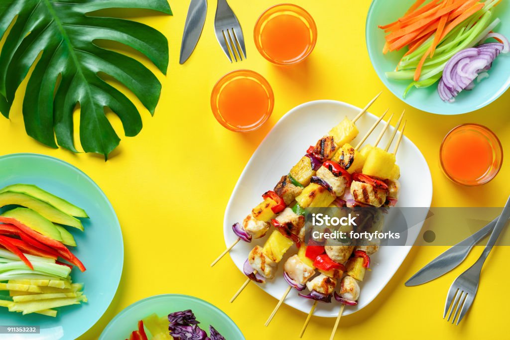 Hawaiian chicken grilled kabob summer food concept Summer simple recipe for grilling, hawaiian chicken kabobs served with freshly diced vegetables and some orange drink in glasses, view from above Summer Stock Photo