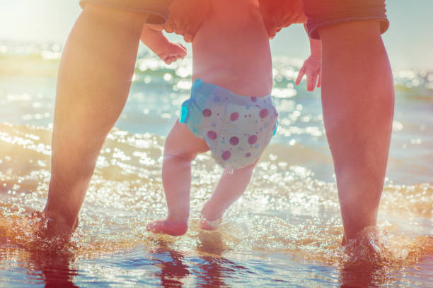 istock Father and baby's feet in waves on summer beach 911363390