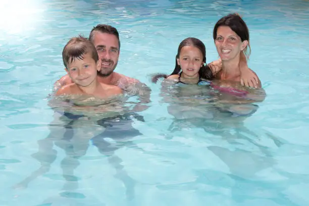 Photo of Family of 4 with two children girls and boys have fun in the pool