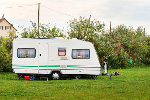 Caravan trailer on a green lawn under the trees in camping, on a sunny Autumn day in France