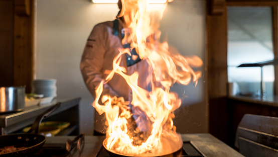 Flames bursting from a pan inside a restaurant kitchen