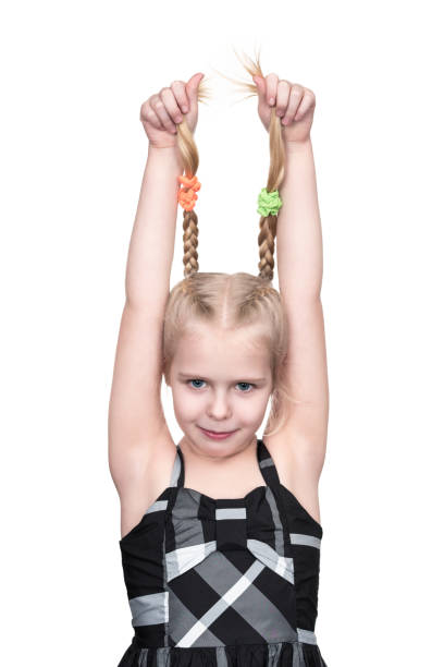 Little girl grabbed herself by pigtails and raised her hands up, isolated on white background