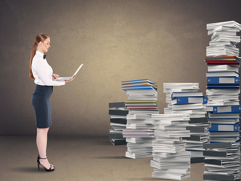 Businesswoman working on laptop by stack of office files