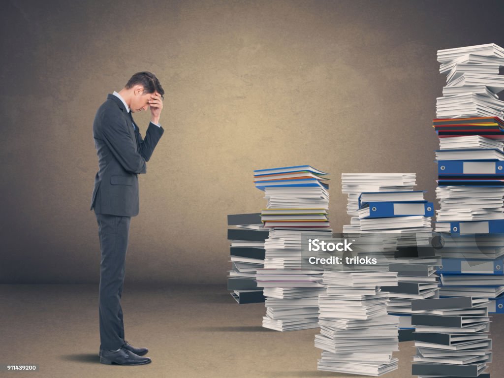 Businessman in despair Tired businessman with stack of office files Paper Stock Photo