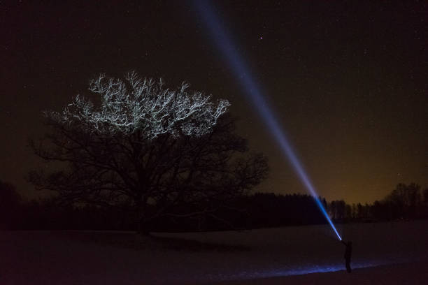 istock Man standing outdoors at night in winter landscape shining with flashlight at sky 911468988