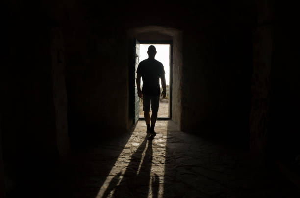 istock Man standing in door way with light and shadows casting on floor 911469264