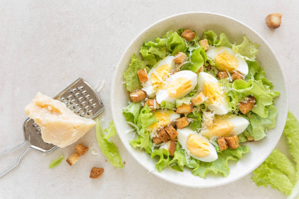istock Caesar salad with eggs, lettuce and parmesan cheese on plate. Top view 911477856