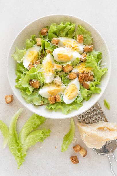istock Caesar salad with eggs, lettuce and parmesan cheese on plate. Top view 911477966