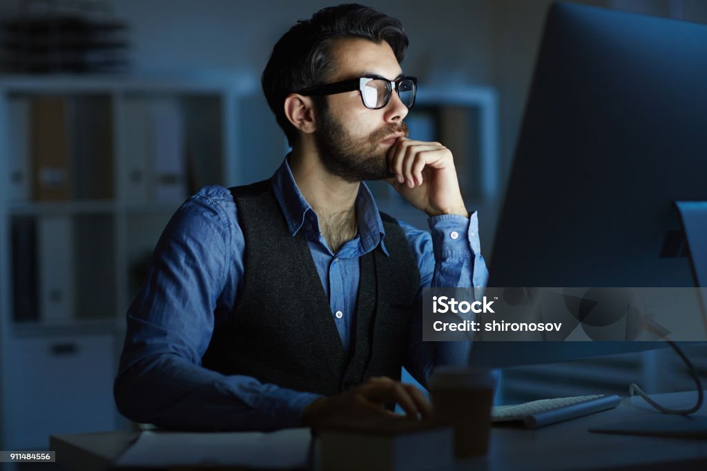 Man working at night Concentrated entrepreneur or manager sitting by desk in front of computer monitor while working at night Night Stock Photo