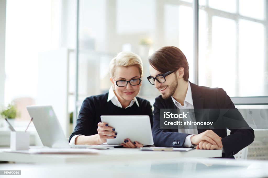 Online training Contemporary employees with digital tablet watching video conference or online seminar while sitting in office Digital Tablet Stock Photo