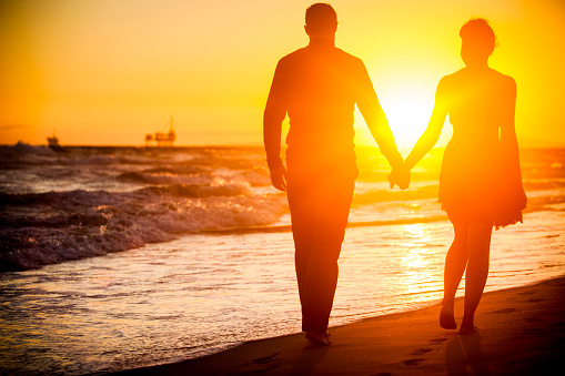 A beautiful diverse couple gets engaged at sunset, walking along the beach