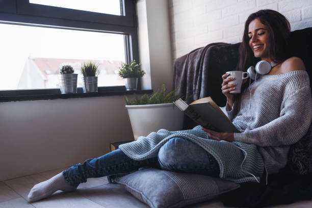 istock Beautiful young woman at home drinking coffee reading a book 911506074