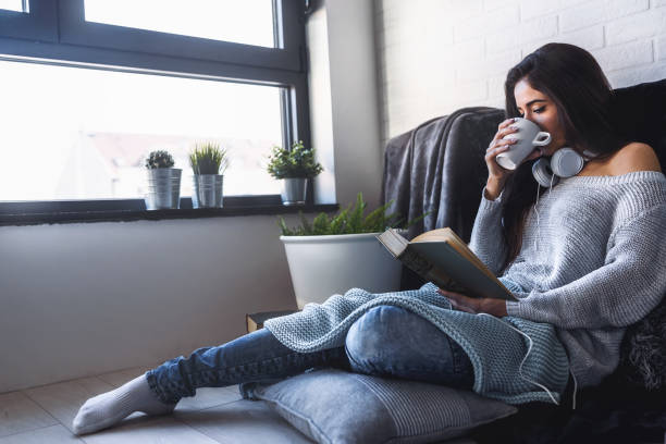 istock Beautiful young woman at home drinking coffee reading a book 911506302