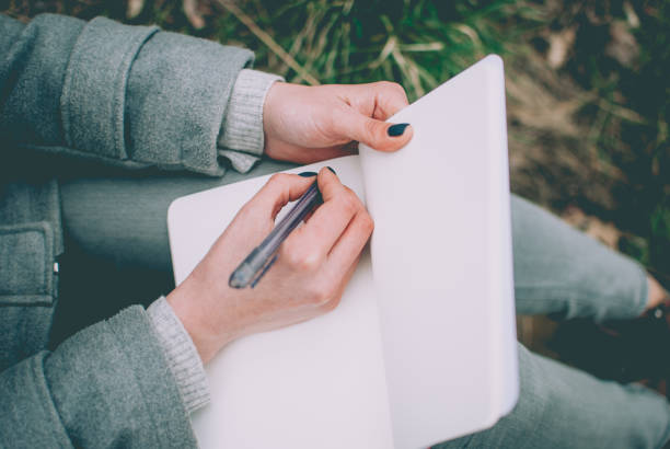 istock Redhead girl sitting on green spring grass and writing 911526552