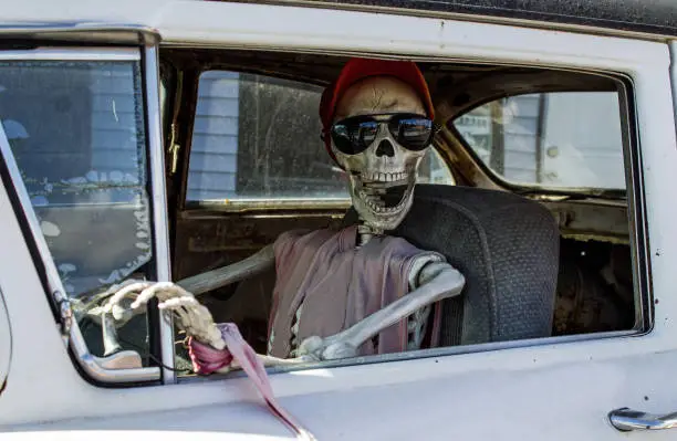 Photo of Smiling Skeleton in Sunglasses and a Red Baseball Cap Driving a Car