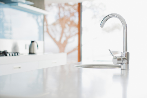Water flowing out of a kitchen stainless steel tap into the sink. Wasting water by leaving a chrome faucet tap running