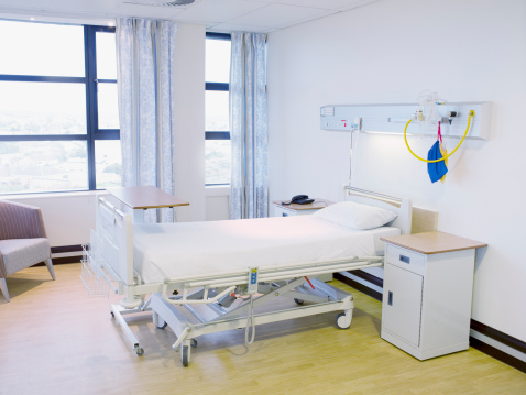 Interior of modern hospital ward with beige and wooden walls, tiled floor, row of comfortable beds with brown blankets and wooden bedside tables. 3d rendering