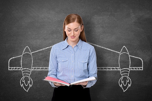 Businesswoman holding diary with aircraft wings drawn on blackboard