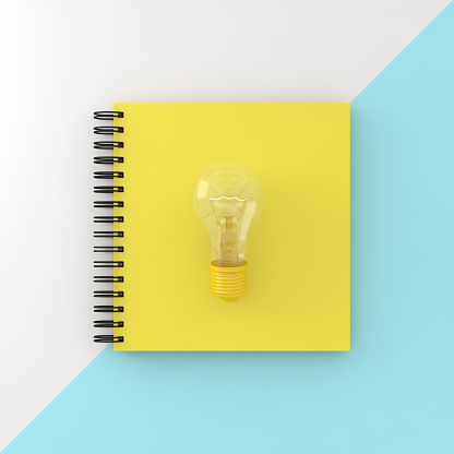 Yellow cover notebook with Light bulb on white and blue pastel background. Top view , flat lay, Minimal work space. The idea about the powerful functions to achieve the goal.