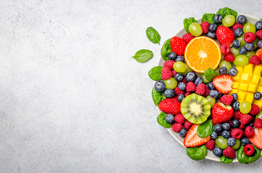 Fruit platter with various fresh strawberry, raspberry, blueberry, tangerine, grape, mango, spinach on a light stone background. Copy space, top view, horizontal image
