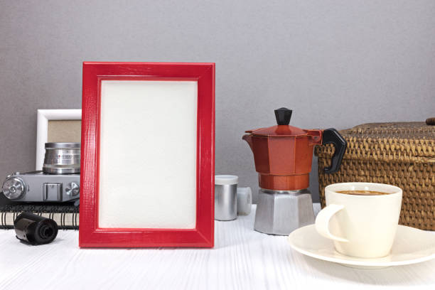 classic camera, empty photo frames, red coffee pot with cup of coffee, old basket on white wooden table