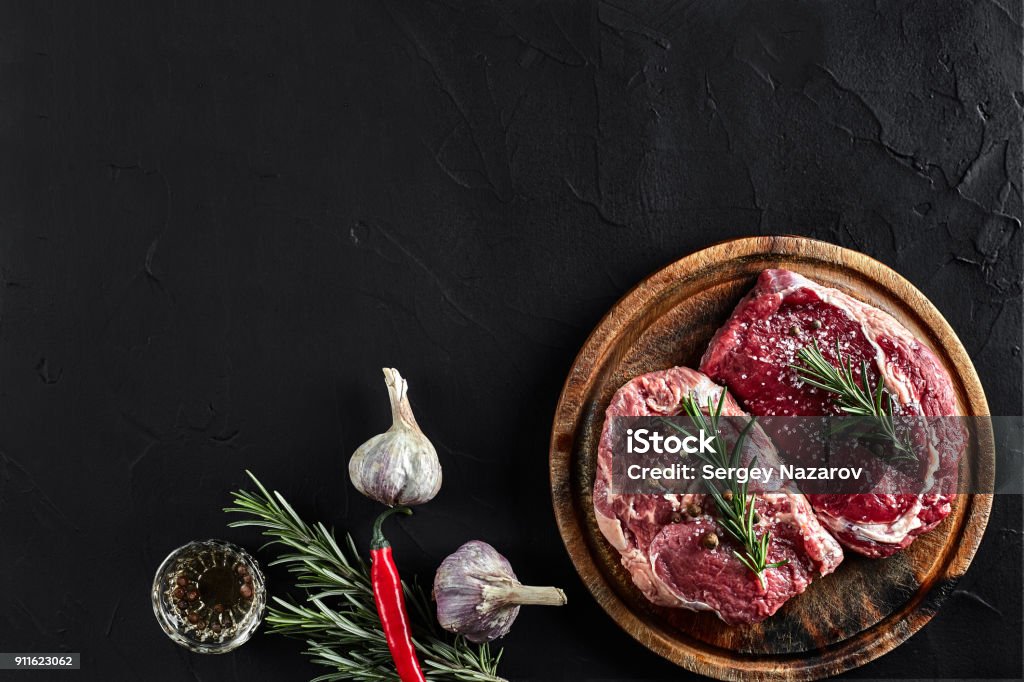 Raw beef steak with spices and ingredients for cooking on cutting board and slate background. Top view Raw beef steak with spices and ingredients for cooking on cutting board and slate background. Top view. Still life. Copy space. Flat lay Meat Stock Photo