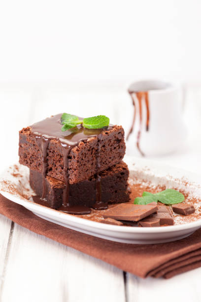 istock Chocolate brownie square pieces in stack on white plate decorated with mint leaves and cocoa powder on white vintage wooden background. American traditional delicious dessert. Close up photography 911640882