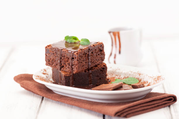 istock Chocolate brownie square pieces in stack on white plate decorated with mint leaves and cocoa powder on white vintage wooden background. American traditional delicious dessert. Close up photography 911640886