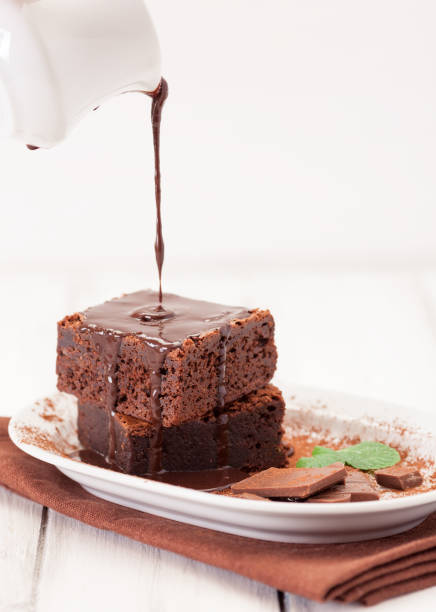 istock Chocolate brownie square pieces in stack on white plate decorated with mint leaves and cocoa powder on white vintage wooden background. American traditional delicious dessert. Close up photography 911640890