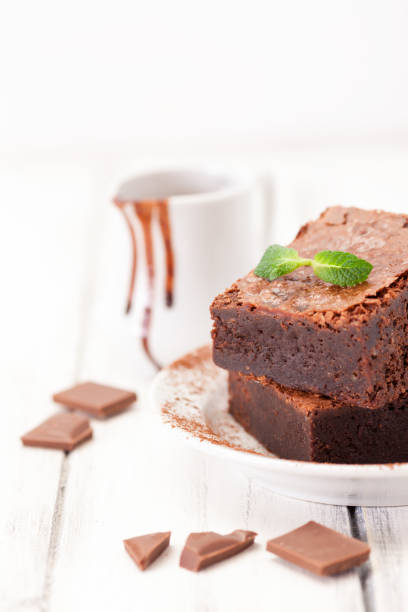 istock Chocolate brownie square pieces in stack on white plate decorated with mint leaves and cocoa powder on white vintage wooden background. American traditional delicious dessert. Close up photography 911640918