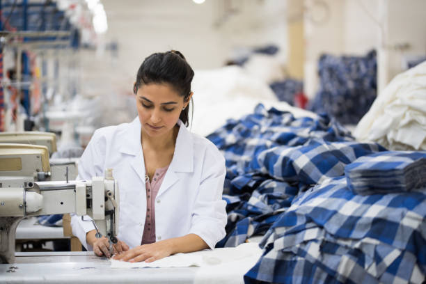 Positive young woman sewing with professional machine at workshop stock photo