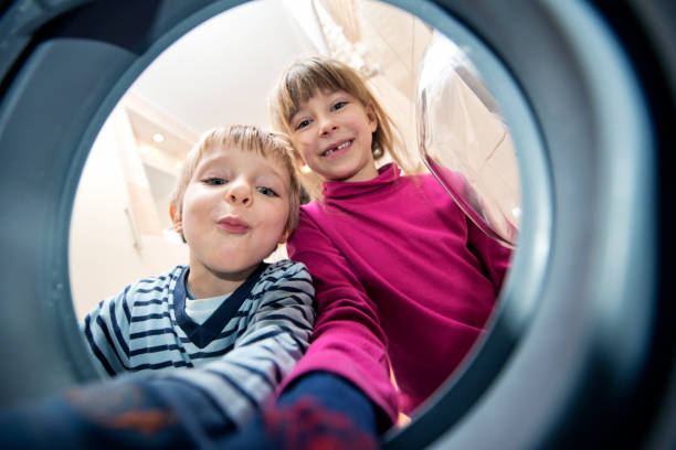 istock Brother and sister unloading a washing machine 911656656