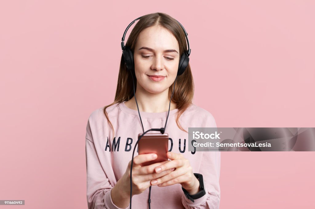 Pretty Young Woman Enjoys Nice Music In Headphones Watches Funny Videos  Types Messages On Cell Phone Dressed Casually Isolated Over Pink Background  People Technology Lifestyle Concept Stock Photo - Download Image Now -