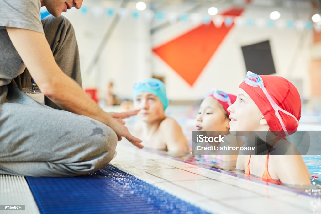 Little learners Cute swimmer and her groupmates in water listening to trainer instructions during training Swimming Stock Photo