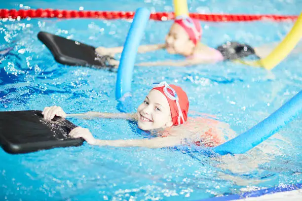 Smiling young swimmer using inflatable resistance pillow while swimming in pool