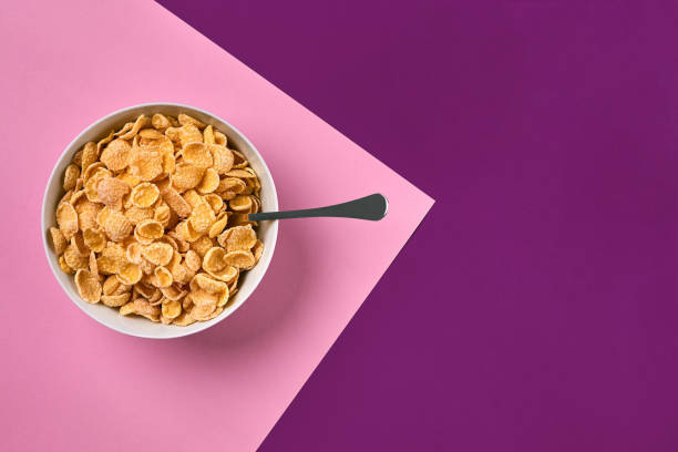 istock Bowl with corn flakes and spoon on purple and pink background, top view 911668826