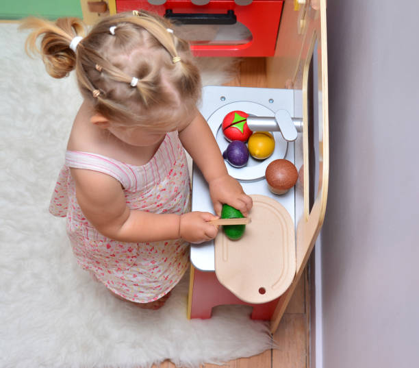 girl cuts wooden vegetables on toy kitchen