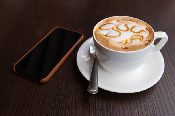 istock Hot latte art coffee cup with mobile phone on wooden table 911678630