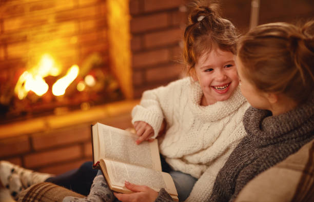 fille famille heureuse pour la mère et l’enfant lire un livre le soir d’hiver près de cheminée - 7653 photos et images de collection